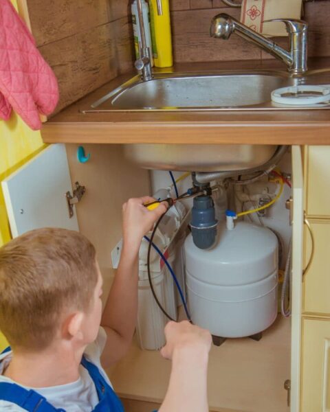 Plumber installing an under-sink water filtration system